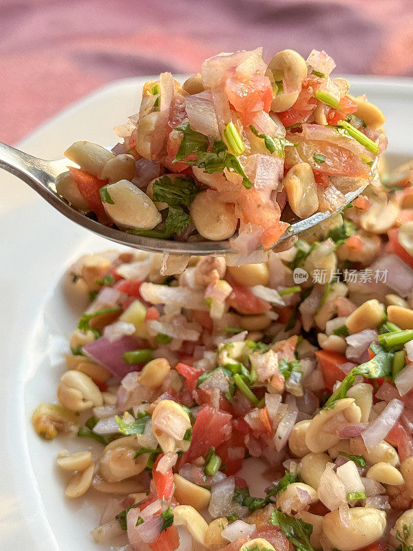 全画幅图像白色碗花生masala chaat，街头风味小吃，花生，chaat masala，辣椒粉，盐，柠檬汁香菜，切成片的serrano胡椒(辣椒)，番茄丁和红洋葱，金属勺食物，桌布